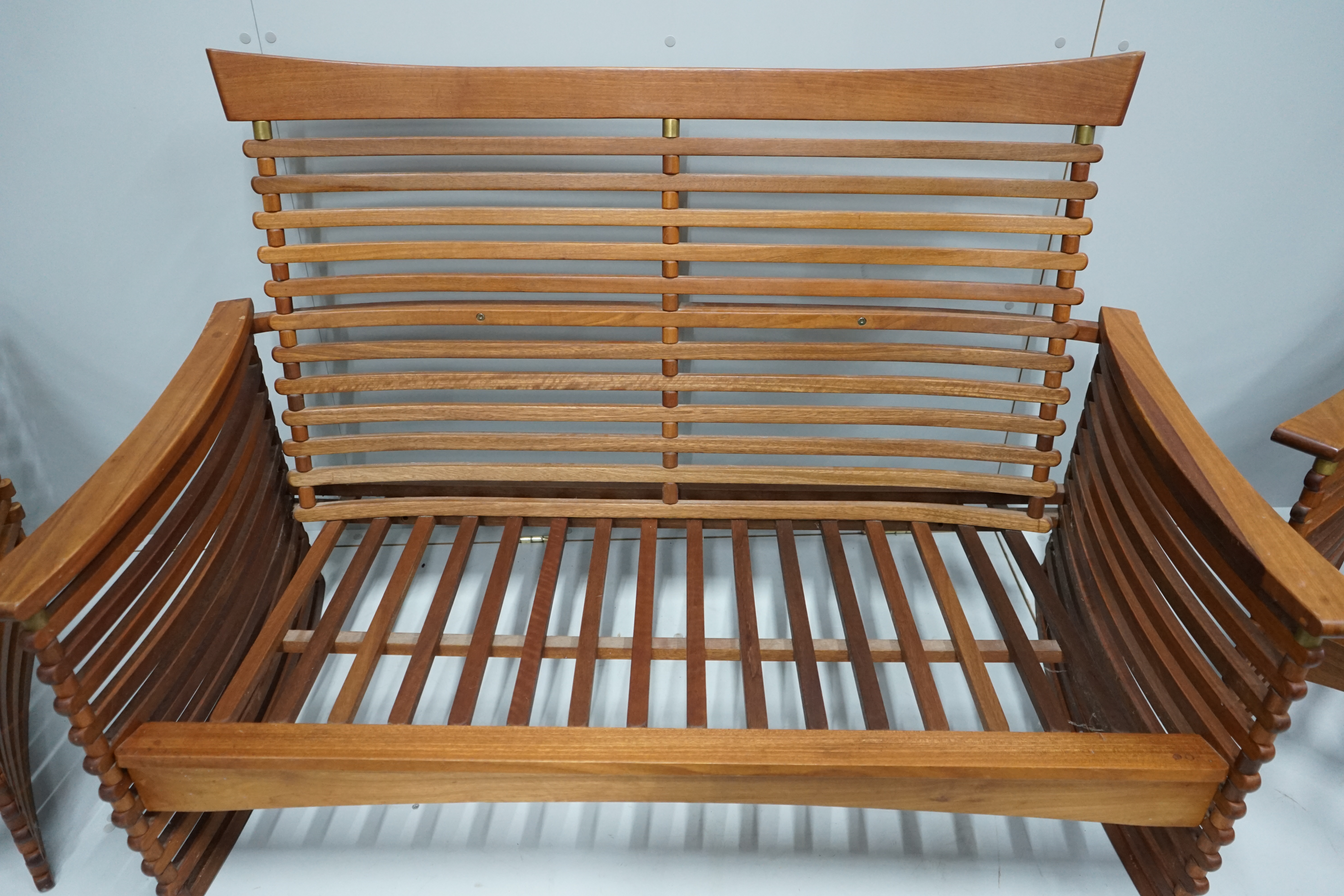 In the manner of Finn Juhl, a Danish brass mounted teak three piece lounge suite of slatted form, settee width 143cm, depth 77cm, height 92cm.